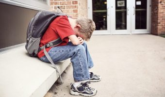 Depressed,Student,Sitting,Outside,Of,School,Hiding,His,Face