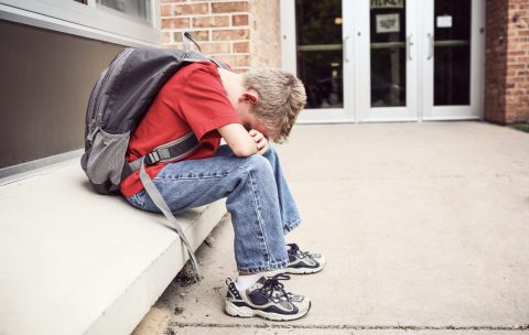 Depressed,Student,Sitting,Outside,Of,School,Hiding,His,Face
